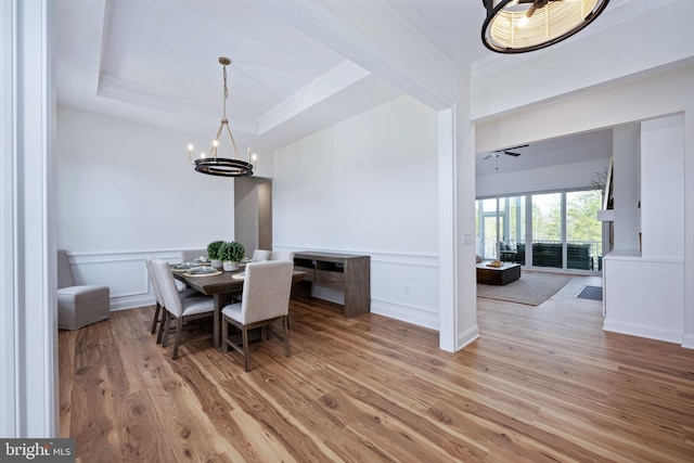 dining area with light wood-type flooring, a tray ceiling, and a chandelier