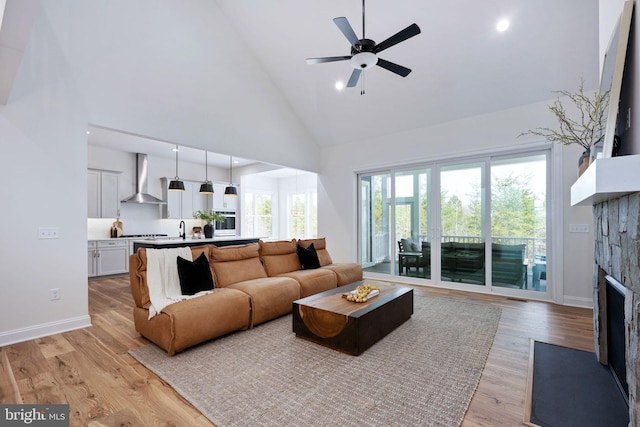 living room featuring high vaulted ceiling, a stone fireplace, light hardwood / wood-style floors, and sink