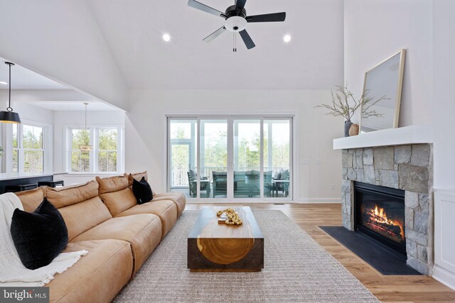 living room with light hardwood / wood-style flooring, ceiling fan, high vaulted ceiling, and a stone fireplace