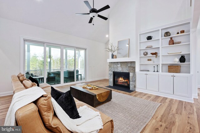 living room with light hardwood / wood-style flooring, built in features, high vaulted ceiling, ceiling fan, and a stone fireplace