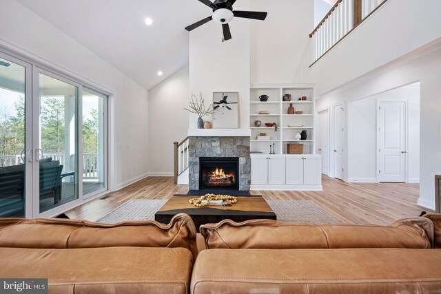 living room with ceiling fan, high vaulted ceiling, light hardwood / wood-style flooring, and a stone fireplace