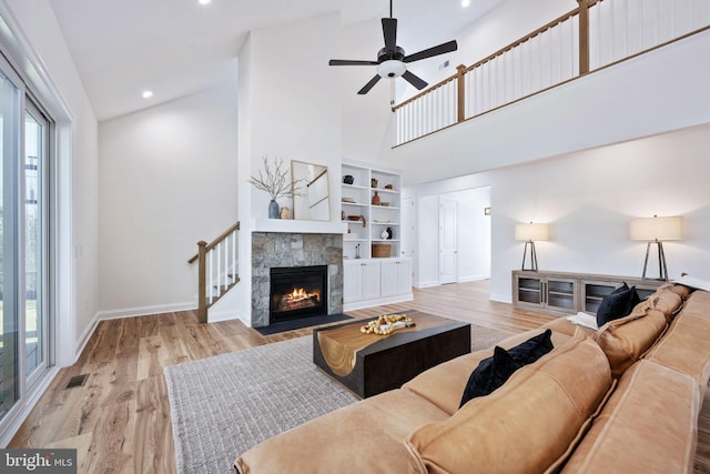 living room with ceiling fan, light wood-type flooring, high vaulted ceiling, and a stone fireplace