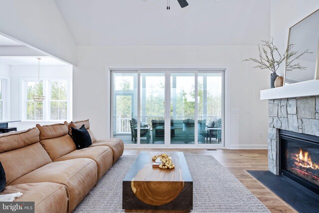 living room featuring light hardwood / wood-style flooring, ceiling fan, a stone fireplace, and lofted ceiling