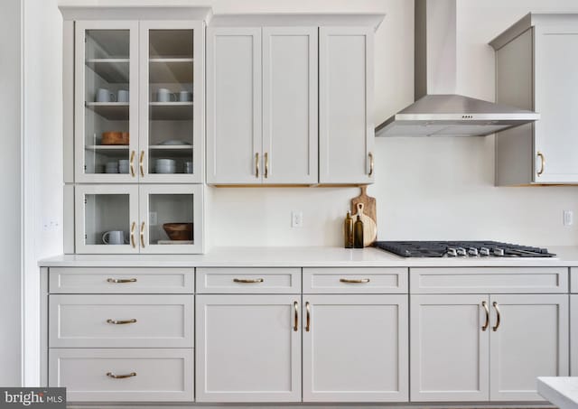 kitchen with stainless steel gas cooktop, white cabinets, and wall chimney exhaust hood