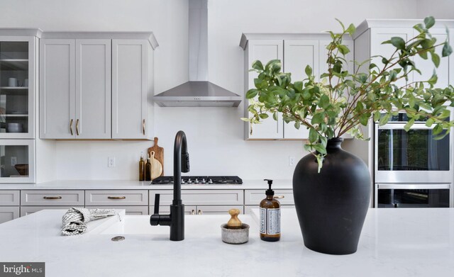 room details featuring wall chimney range hood, light stone counters, and gas cooktop