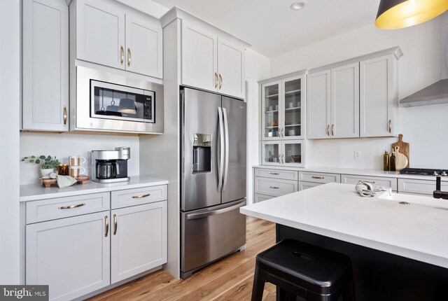 kitchen with light hardwood / wood-style flooring, wall chimney exhaust hood, white cabinets, a breakfast bar, and stainless steel appliances