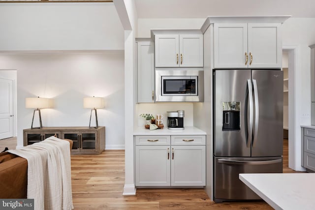 kitchen with stainless steel appliances, white cabinetry, and light hardwood / wood-style flooring