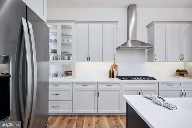 kitchen featuring light wood-type flooring, wall chimney exhaust hood, white cabinets, gas cooktop, and stainless steel fridge