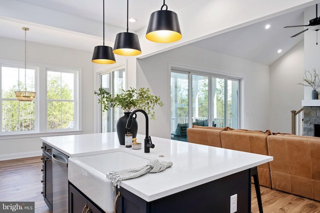 kitchen featuring light wood-type flooring, vaulted ceiling, a stone fireplace, and an island with sink