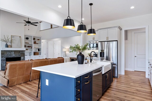 kitchen with light hardwood / wood-style flooring, a kitchen island with sink, blue cabinets, appliances with stainless steel finishes, and a fireplace