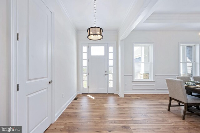 foyer entrance with light hardwood / wood-style flooring, crown molding, and an inviting chandelier