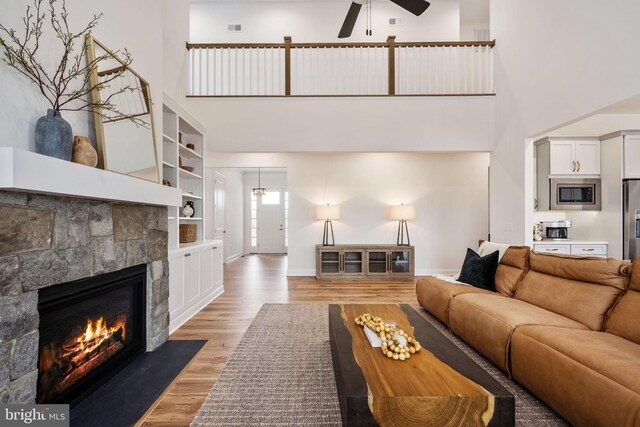 living room featuring ceiling fan, a fireplace, hardwood / wood-style flooring, and a towering ceiling