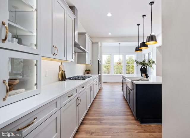 kitchen with hardwood / wood-style floors, decorative light fixtures, sink, stainless steel gas cooktop, and wall chimney exhaust hood