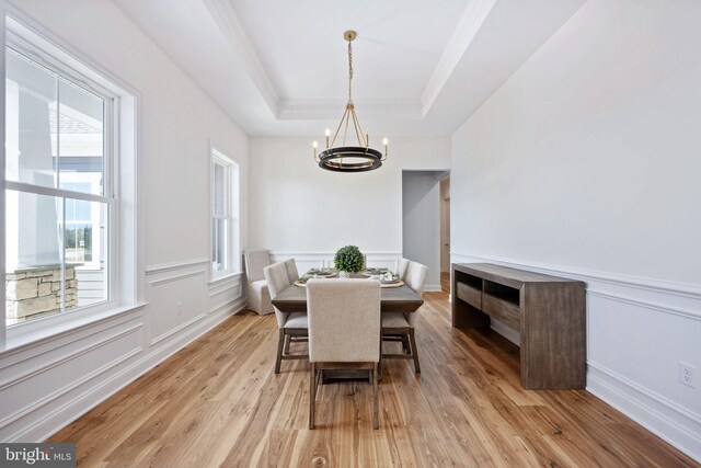 dining space featuring light wood-type flooring, a raised ceiling, and a notable chandelier