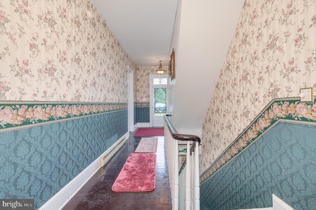 hall with dark wood-style flooring, an upstairs landing, baseboards, baseboard heating, and wallpapered walls