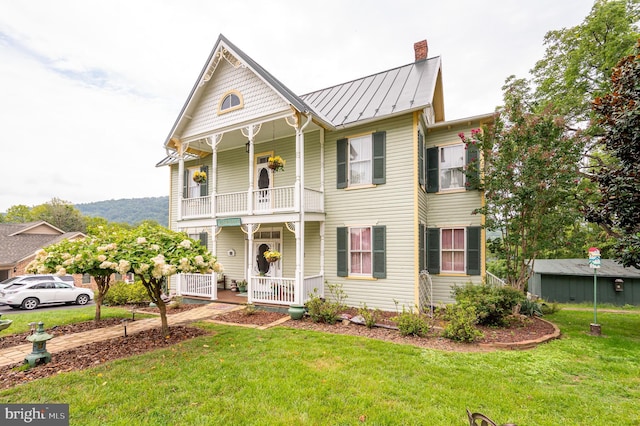 victorian house featuring a balcony, a standing seam roof, a front lawn, and covered porch