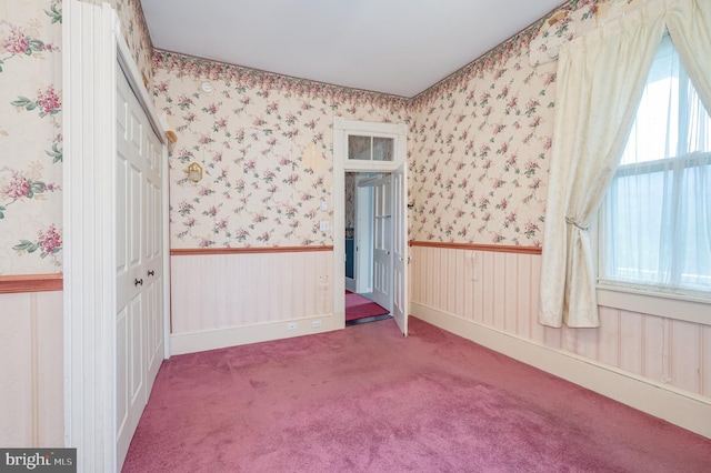 spare room featuring carpet floors, wallpapered walls, and a wainscoted wall