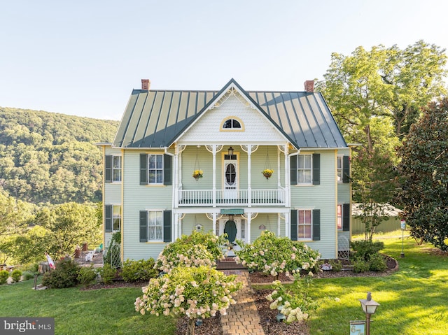 victorian-style house with a standing seam roof, a chimney, and a balcony