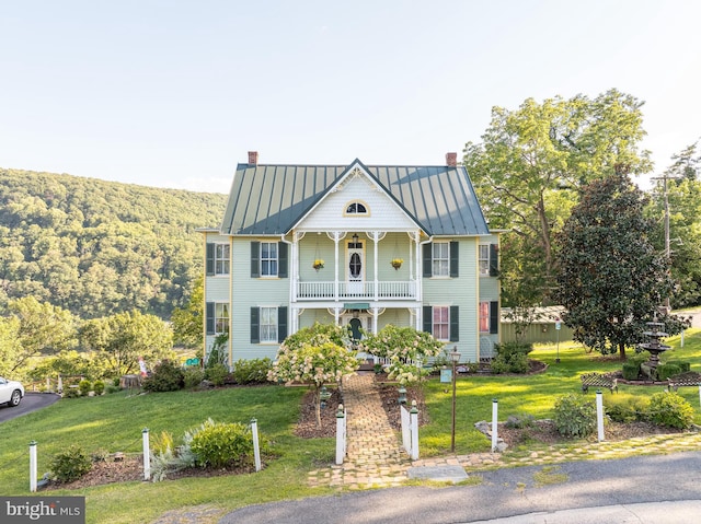 view of front of home featuring a chimney, a standing seam roof, metal roof, a balcony, and a front lawn