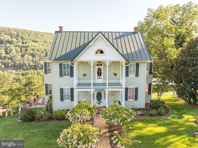 view of front of home with a porch, a standing seam roof, a chimney, and a balcony