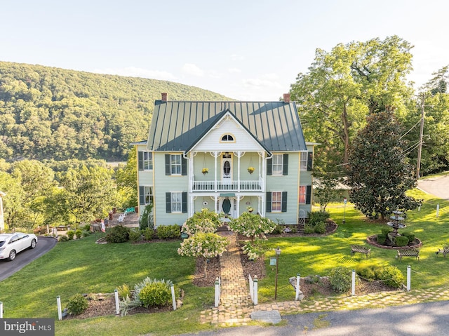 view of front of house with a balcony, a standing seam roof, a chimney, and metal roof