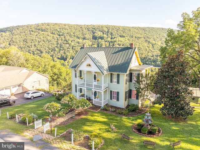 view of front of property featuring metal roof, a balcony, a standing seam roof, a chimney, and a view of trees