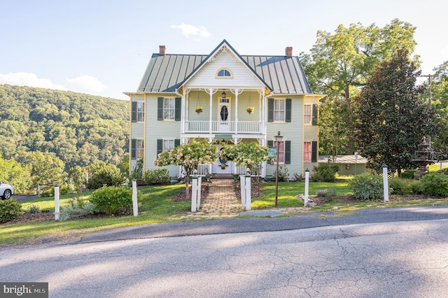 view of front of house featuring metal roof, a balcony, covered porch, a standing seam roof, and a chimney