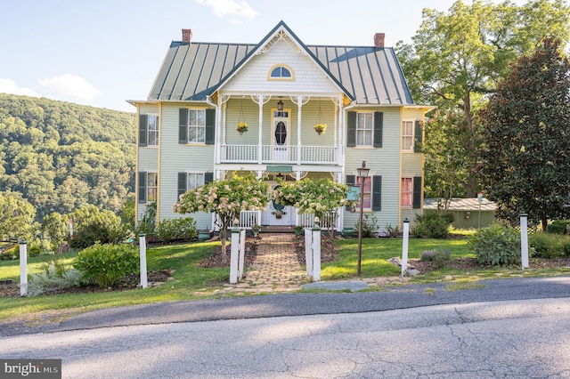 victorian home featuring a front yard, a standing seam roof, metal roof, and a chimney