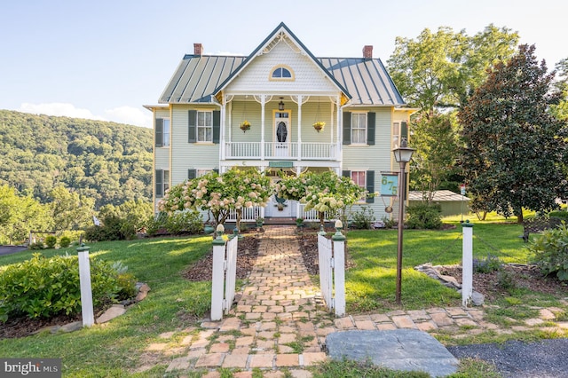 victorian home with a standing seam roof, a chimney, a porch, and a front yard