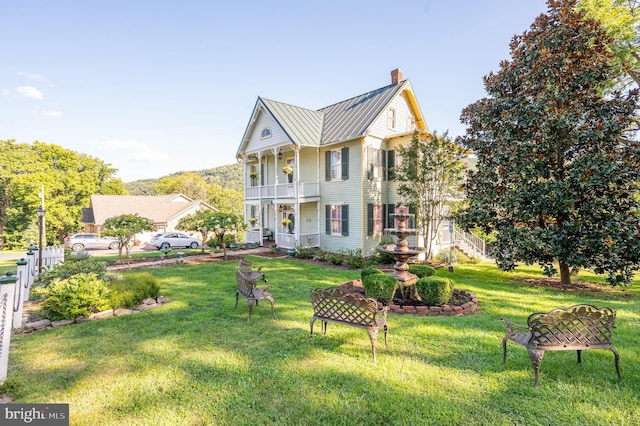 view of front of house featuring metal roof, a front lawn, a standing seam roof, and a balcony