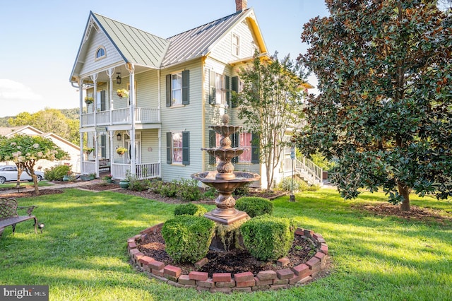 view of front facade featuring a balcony, a chimney, a porch, a standing seam roof, and a front lawn