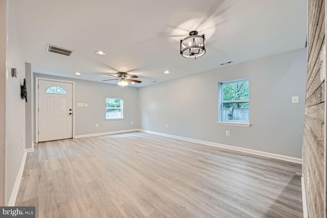 unfurnished living room featuring ceiling fan with notable chandelier, a wealth of natural light, and light hardwood / wood-style floors