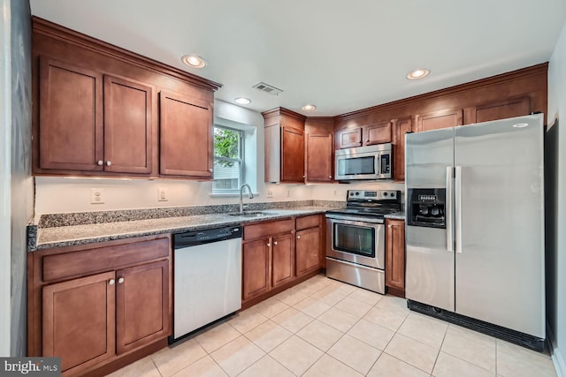 kitchen featuring dark stone countertops, light tile patterned floors, appliances with stainless steel finishes, and sink