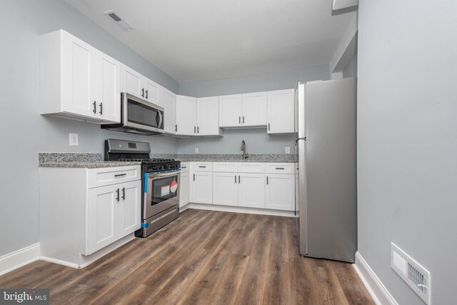 kitchen featuring sink, white cabinetry, stainless steel appliances, light stone counters, and dark hardwood / wood-style flooring