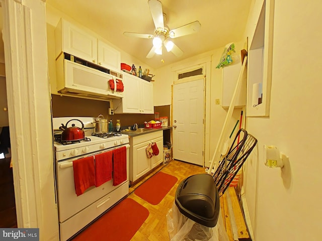 kitchen featuring white gas range, dark countertops, a ceiling fan, white cabinetry, and a sink