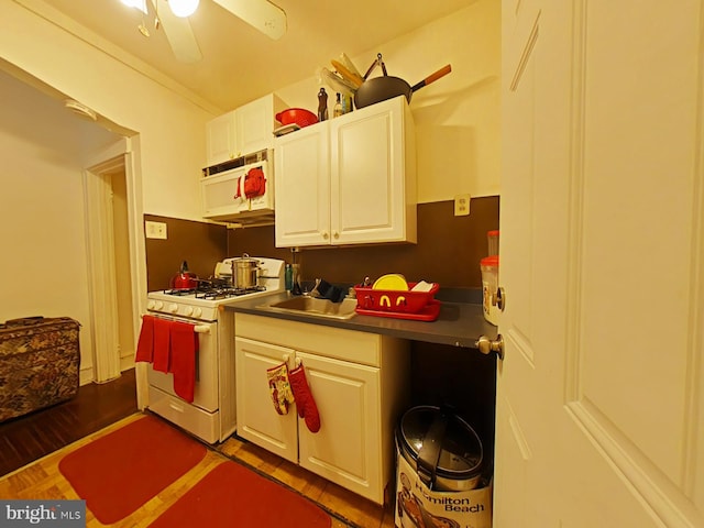 kitchen featuring dark wood finished floors, white cabinets, a sink, ceiling fan, and white appliances