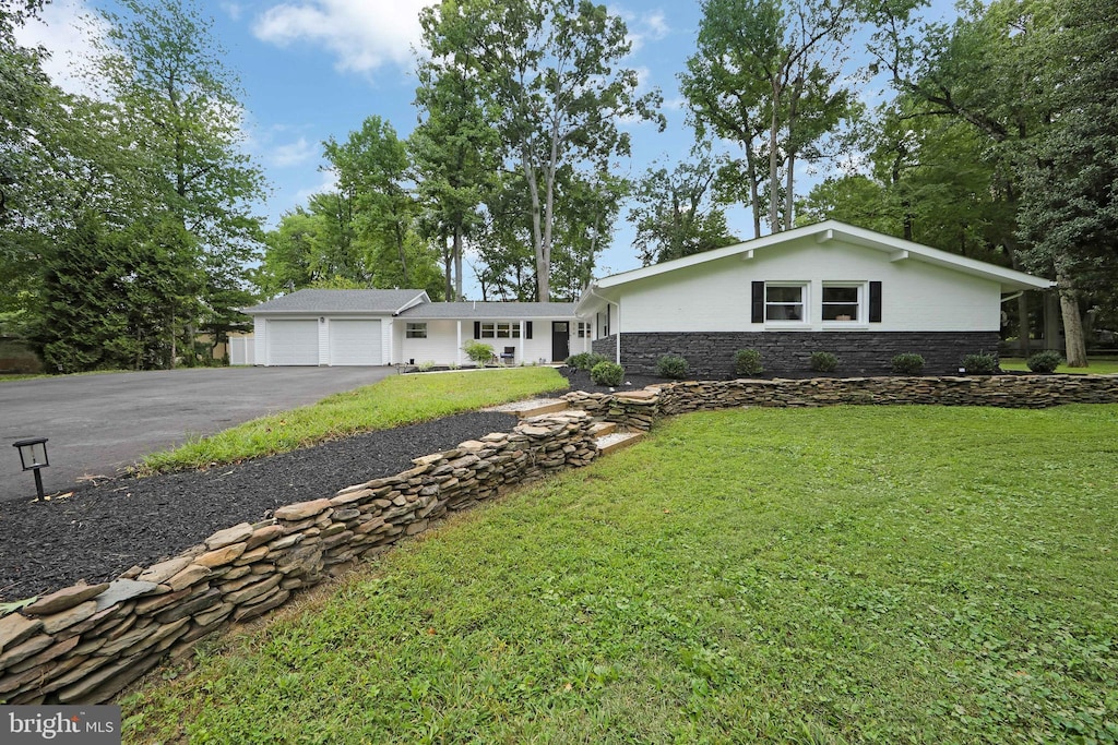 view of front of home with aphalt driveway, stucco siding, a front yard, a garage, and stone siding