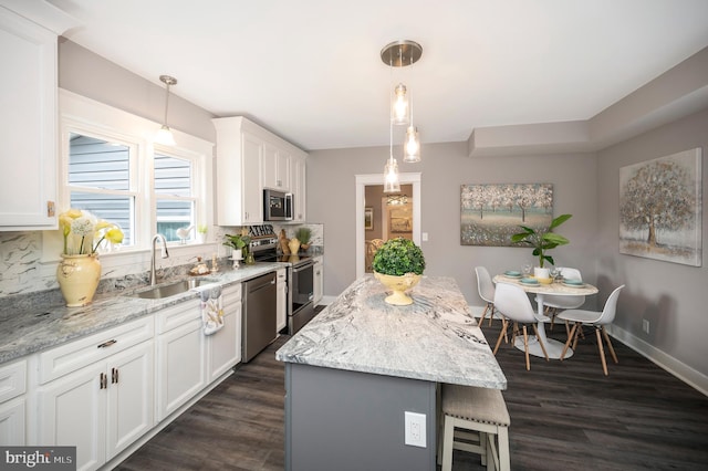 kitchen with sink, appliances with stainless steel finishes, white cabinets, a kitchen island, and decorative light fixtures