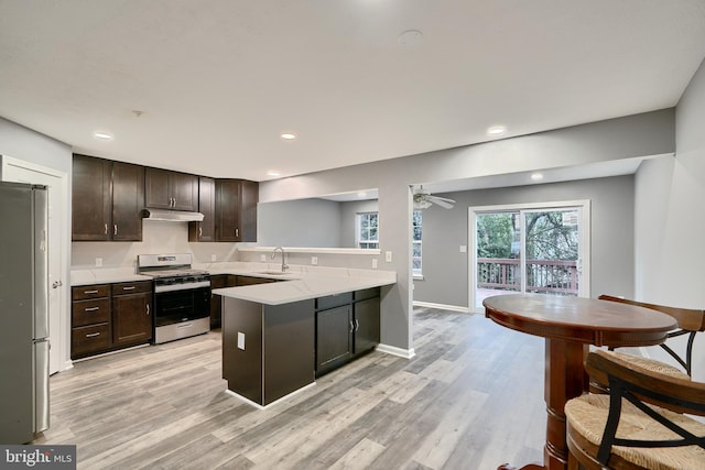 kitchen featuring appliances with stainless steel finishes, light hardwood / wood-style flooring, dark brown cabinetry, kitchen peninsula, and ceiling fan