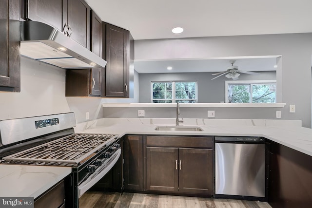 kitchen with stainless steel appliances, sink, light stone counters, wood-type flooring, and ceiling fan