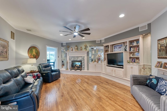 living room with a premium fireplace, ceiling fan, light hardwood / wood-style flooring, and crown molding