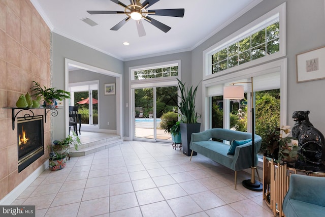 interior space featuring crown molding, a tile fireplace, light tile patterned floors, and ceiling fan