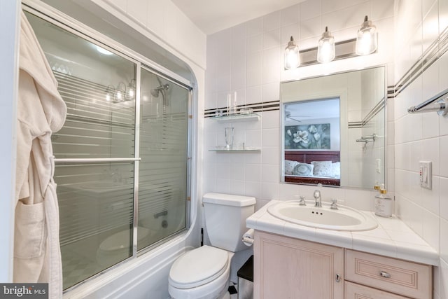 full bathroom with tile walls, decorative backsplash, vanity, bath / shower combo with glass door, and toilet