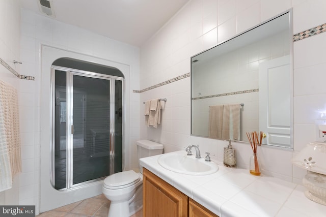 bathroom with vanity, tile walls, toilet, and a shower with door