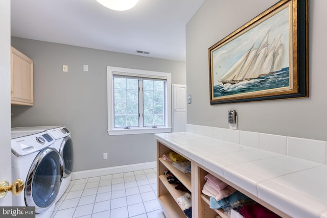 laundry room featuring washing machine and dryer, light tile patterned floors, and cabinets