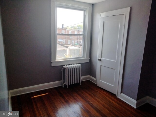 unfurnished room featuring dark hardwood / wood-style flooring and radiator heating unit