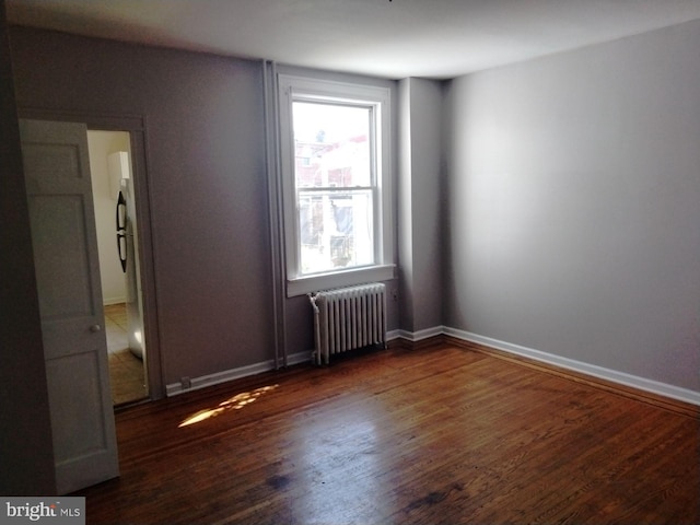 unfurnished room with radiator heating unit, dark wood-type flooring, and a wealth of natural light