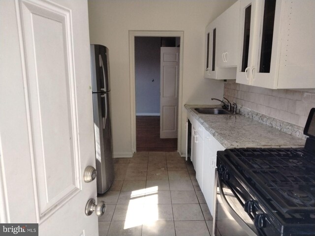 kitchen featuring light tile patterned flooring, tasteful backsplash, white cabinetry, stainless steel fridge, and stove