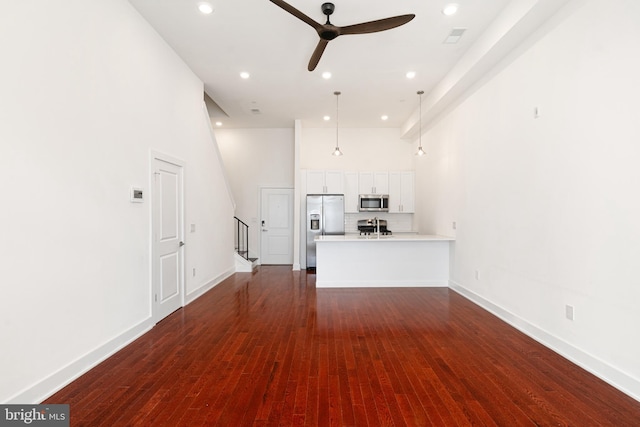 unfurnished living room featuring dark hardwood / wood-style flooring, ceiling fan, and a towering ceiling