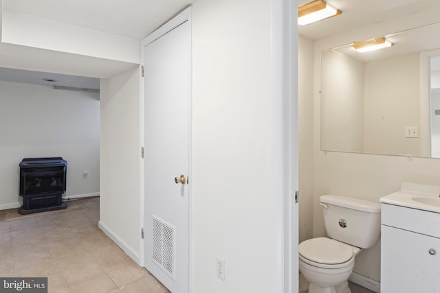 bathroom with tile patterned floors, vanity, a wood stove, and toilet